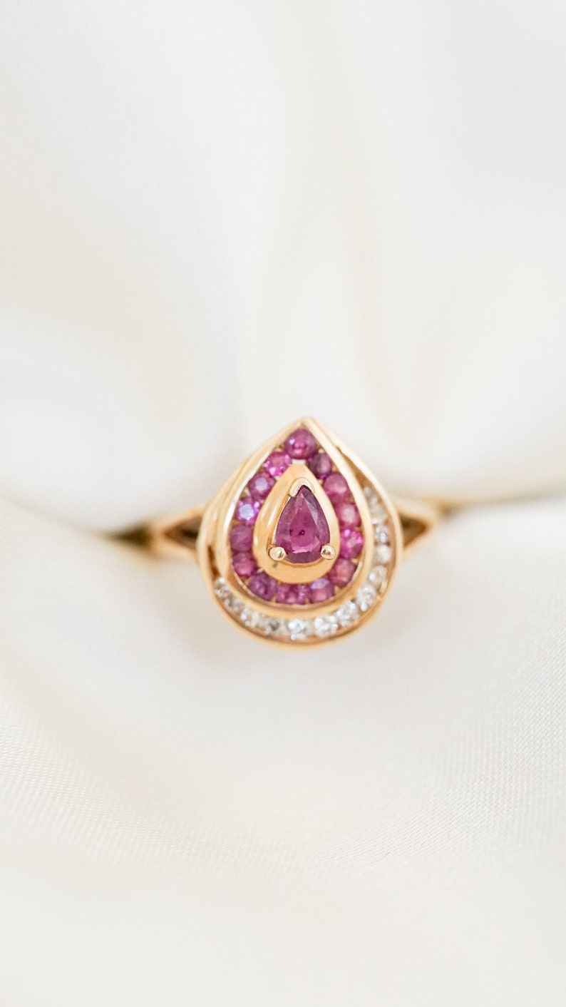 May include: A gold ring with a pear-shaped pink gemstone surrounded by smaller pink gemstones and a halo of white gemstones.