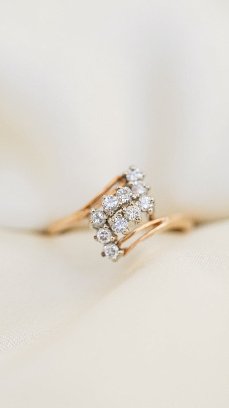 Pode incluir: Um anel de ouro com um aglomerado de pequenos diamantes engastados em uma banda ondulada.