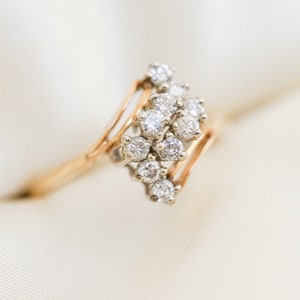 Pode incluir: Um anel de ouro com um grupo de pequenos diamantes engastados em um design delicado e curvo.