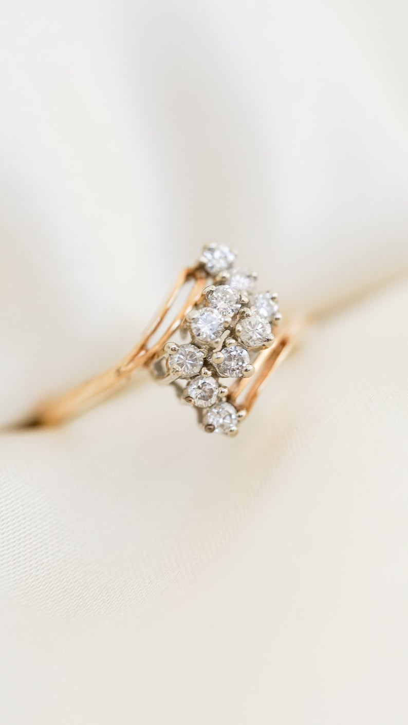 Pode incluir: Um anel de ouro com um grupo de pequenos diamantes engastados em um design delicado e curvo.