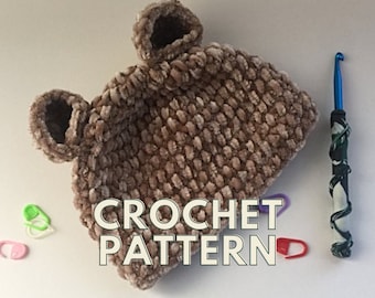 May include: A brown crocheted hat with bear ears and the text "CROCHET PATTERN" on a white surface.