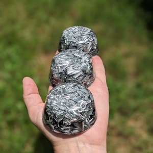 Op de afbeelding: Drie ronde, zilveren en zwarte kristallen bollen die op elkaar gestapeld zijn. De bollen zijn gemaakt van helder kristal met zilveren vlokken.