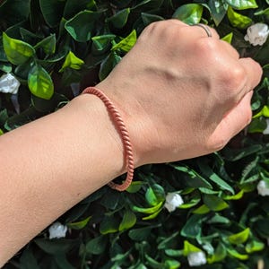 Puede incluir: Un brazalete de alambre de cobre con un diseño trenzado. El brazalete se lleva en la muñeca.