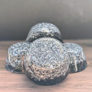 May include: Four black, dome-shaped objects with a metallic, silver-coloured, crystalline interior. The objects are arranged on a wooden surface. The crystalline material reflects light, creating a sparkling effect. The objects appear to be decorative or functional.