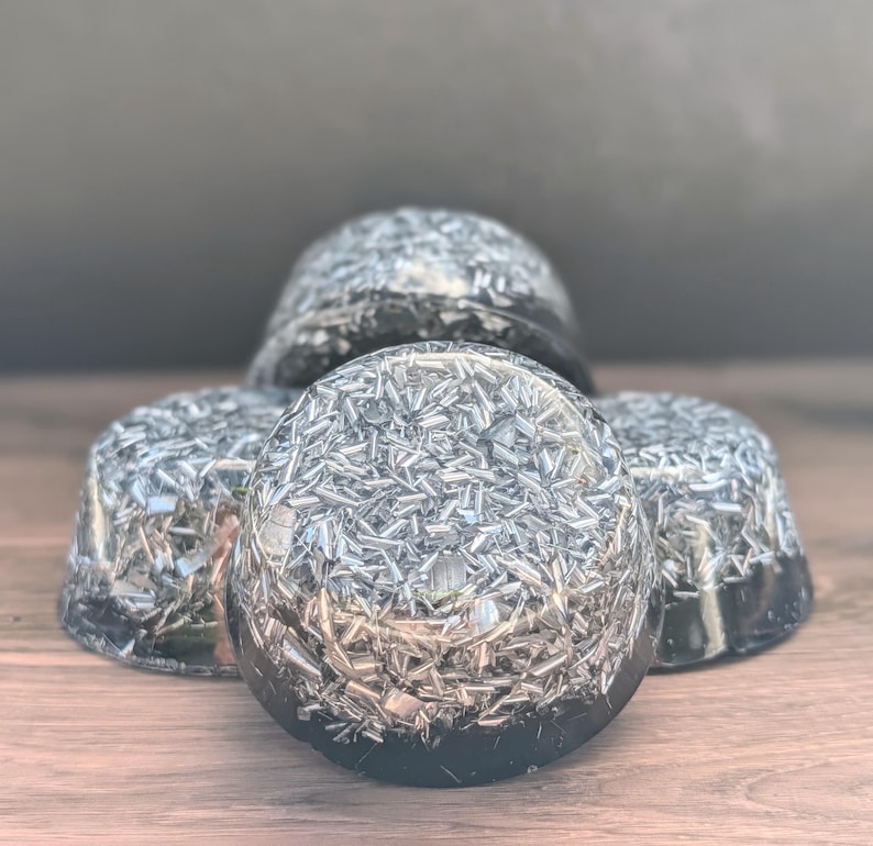 May include: Four black, dome-shaped objects with a metallic, silver-coloured, crystalline interior. The objects are arranged on a wooden surface. The crystalline material reflects light, creating a sparkling effect. The objects appear to be decorative or functional.