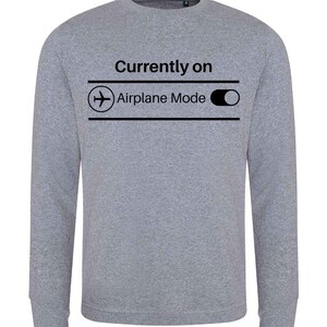 May include: A heather gray sweatshirt with the text "Currently on Airplane Mode" in black. The design includes an airplane icon and a toggle switch graphic, suggesting a playful reference to technology and travel.