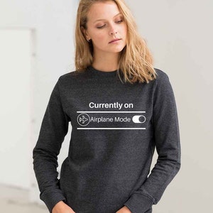 May include: Dark gray sweatshirt with the text "Currently on Airplane Mode" in white. The design includes an airplane icon and a toggle switch graphic. The long-sleeved crew neck top is made of a soft material.