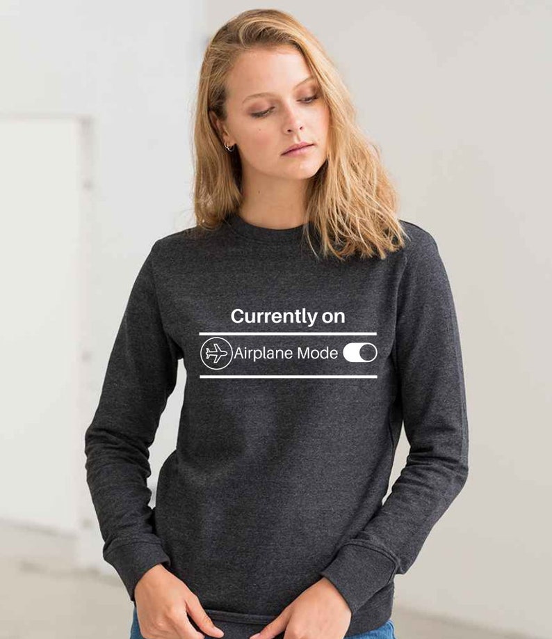 May include: Dark gray sweatshirt with the text "Currently on Airplane Mode" in white. The design includes an airplane icon and a toggle switch graphic. The long-sleeved crew neck top is made of a soft material.
