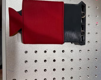 May include: A red leather wallet with a black plastic case attached to it. The wallet has a flap with a triangular shape.