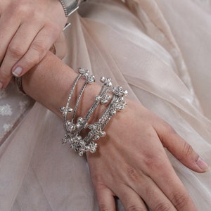 Op de afbeelding: Een set zilveren armbanden met decoratieve kralen. De armbanden zijn gestapeld op de pols van een persoon.