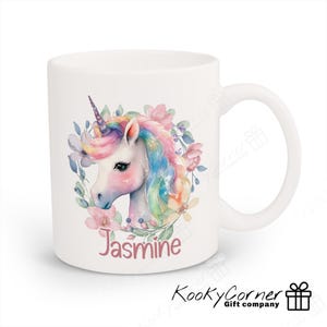 May include: White ceramic mug featuring a watercolour illustration of a unicorn with a rainbow mane and flowers. The name "Jasmine" is printed in pink below the unicorn.