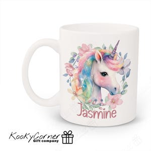 May include: White ceramic mug featuring a watercolour illustration of a unicorn with a rainbow mane and tail, surrounded by pink and purple flowers. The name "Jasmine" is written in pink below the unicorn.