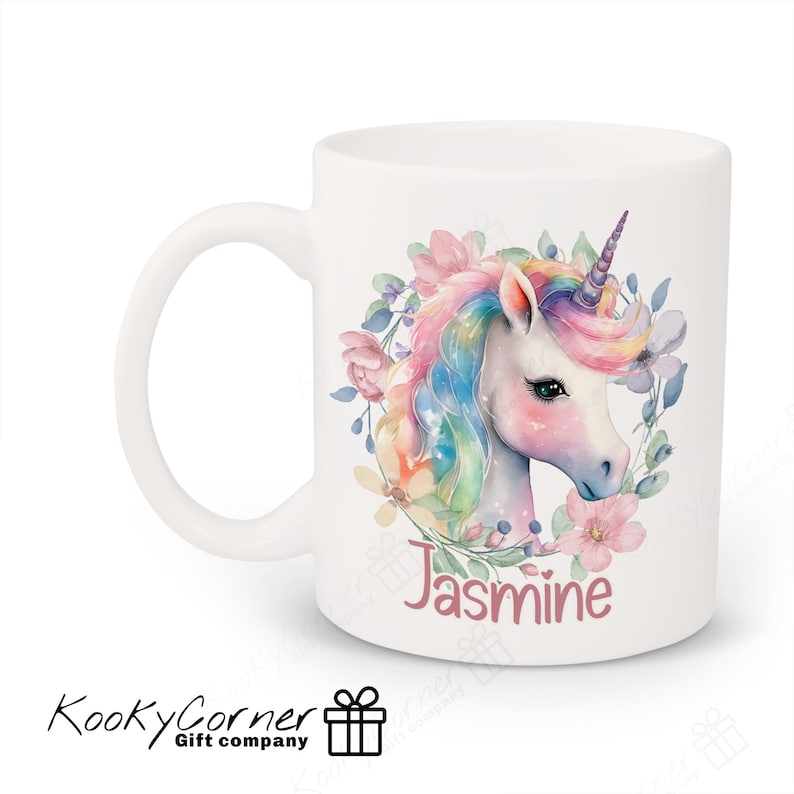 May include: White ceramic mug featuring a watercolour illustration of a unicorn with a rainbow mane and tail, surrounded by pink and purple flowers. The name "Jasmine" is written in pink below the unicorn.