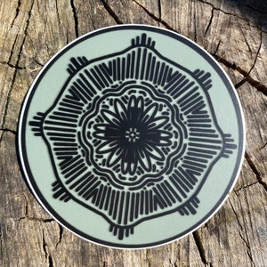 May include: A round sticker with a black and white mandala design on a light green background.