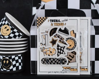 May include: A party favor box with a black and white checkered pattern. The box contains a set of temporary tattoos with a skateboard, lightning bolts, stars, and smiley faces. The box also has the text "Young, Wild & Three" and "Tattoos" on it.