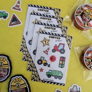 May include: A selection of construction-themed party items. Includes stickers, cards with the text "CARTER is three", and cookies with a photo and the text "I HOPE YOU HAD LOADS OF FUN!" on them. The items are on a yellow background.