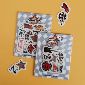 May include: Two packs of stickers with a grey and white chequered pattern, featuring music-themed designs. Individual stickers include a guitar, stars, and the text "WARPED TOUR". The background is a solid yellow.