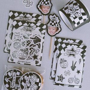Puede incluir: Un conjunto de art&iacute;culos para fiestas con un patr&oacute;n de cuadros blanco y negro y un dise&ntilde;o de calavera y huesos cruzados. El conjunto incluye un adorno para cupcake, una hoja de pegatinas, una bolsa de regalo con una galleta y un vaso de papel. El texto en los art&iacute;culos dice "Bad to the Bone".