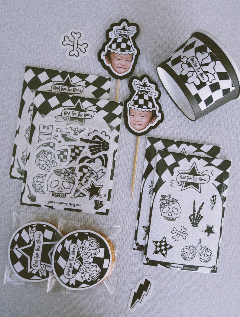 Puede incluir: Un conjunto de art&iacute;culos para fiestas con un patr&oacute;n de cuadros blanco y negro y un dise&ntilde;o de calavera y huesos cruzados. El conjunto incluye un adorno para cupcake, una hoja de pegatinas, una bolsa de regalo con una galleta y un vaso de papel. El texto en los art&iacute;culos dice "Bad to the Bone".