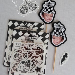 Puede incluir: Un conjunto de tatuajes temporales en blanco y negro con un tema de calavera y huesos cruzados. Los tatuajes est&aacute;n empaquetados en una bolsa de pl&aacute;stico transparente con un fondo a cuadros blanco y negro. La bolsa tambi&eacute;n incluye una tarjeta peque&ntilde;a con el texto "Bad two the Bone" y una direcci&oacute;n de sitio web.