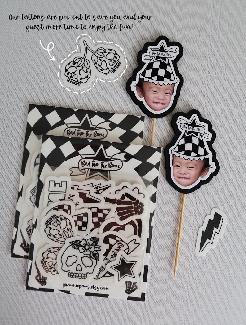 Puede incluir: Un conjunto de tatuajes temporales en blanco y negro con un tema de calavera y huesos cruzados. Los tatuajes est&aacute;n empaquetados en una bolsa de pl&aacute;stico transparente con un fondo a cuadros blanco y negro. La bolsa tambi&eacute;n incluye una tarjeta peque&ntilde;a con el texto "Bad two the Bone" y una direcci&oacute;n de sitio web.