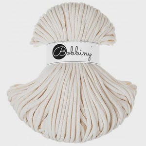 Può includere: Un gomitolo color crema di cordoncino per macramè Bobbiny. Il cordoncino è avvolto strettamente e tenuto insieme da un'etichetta bianca con il logo e il testo Bobbiny. Adatto a vari progetti di artigianato.