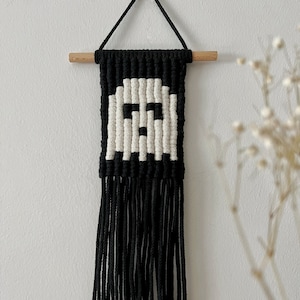 Könnte beinhalten: Schwarzer und weißer Makramee-Wandbehang mit geometrischem Muster und Fransen.