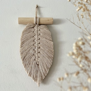 May include: A beige macrame feather wall hanging with a wooden dowel at the top.