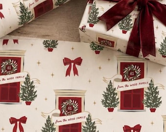 May include: Wrapping paper featuring a repeating pattern of red doors with wreaths labeled 61, green potted pine trees, and red bows. A banner across each door reads from the WOOD FAMILY. A gift box is wrapped in the same paper with a dark red velvet bow.