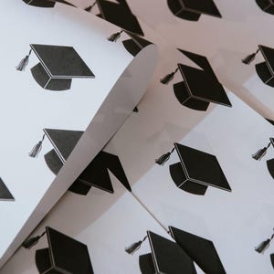 May include: A stack of white paper sheets with a black graduation cap design repeated across the surface.