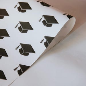 May include: White wrapping paper with a repeating pattern of black graduation caps.