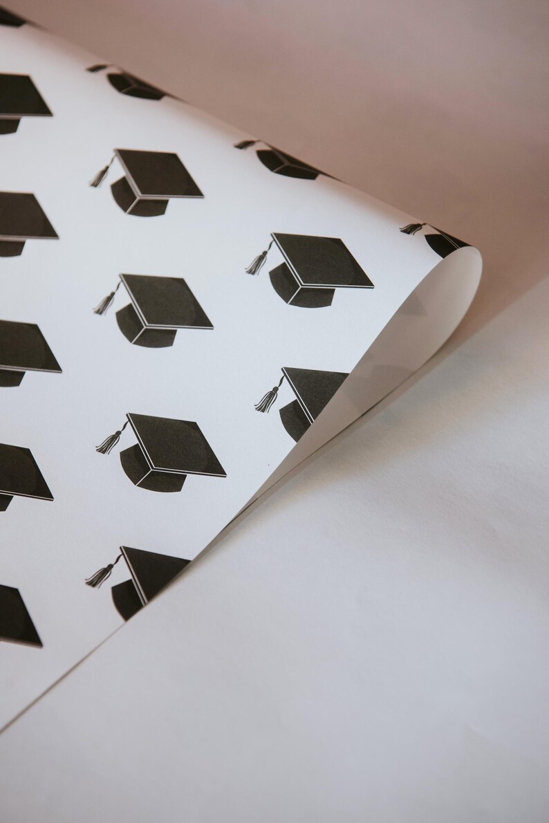 May include: White wrapping paper with a repeating pattern of black graduation caps.