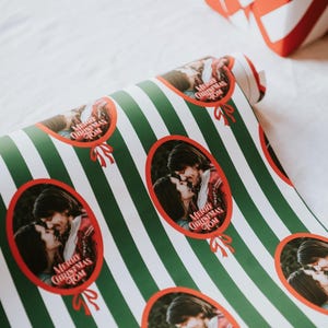 May include: A roll of wrapping paper featuring a pattern of vertical dark green and white stripes. The paper is decorated with repeating oval frames in red, each containing a photograph of a couple and the text Merry Christmas Tom.
