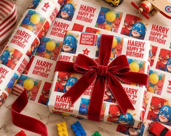 May include: A gift wrapped in white paper featuring a repeating pattern of Spider-Man and Captain America masks with the text Harry Happy 3rd Birthday, tied with a dark red velvet ribbon, surrounded by toy cars, a wooden plane, and plastic bricks.