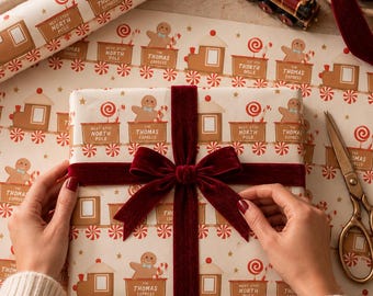 May include: A rectangular gift wrapped in cream-colored paper featuring a repeating pattern of brown train cars, gingerbread figures, red and white peppermint candies, and gold stars. The text reads The Thomas Express and Next Stop North Pole.