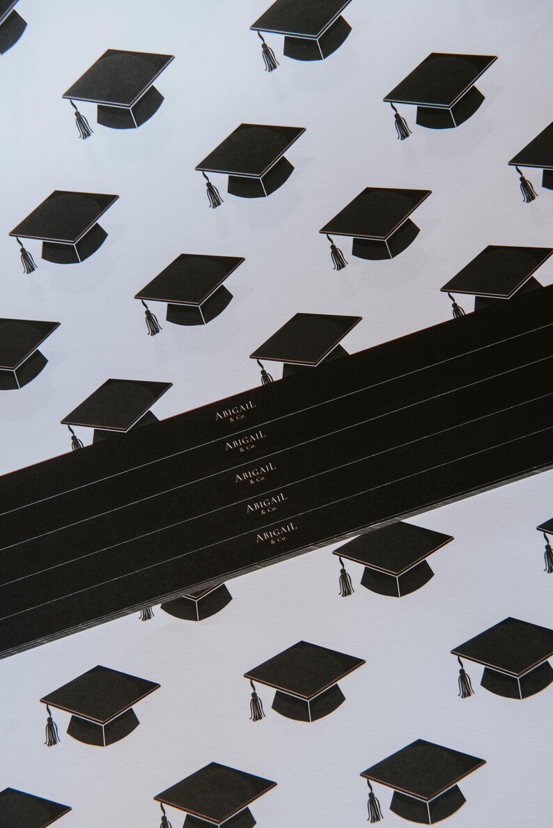 May include: Black and white graduation cap pattern wrapping paper with the text "Abigail & Co." repeated on a black strip.