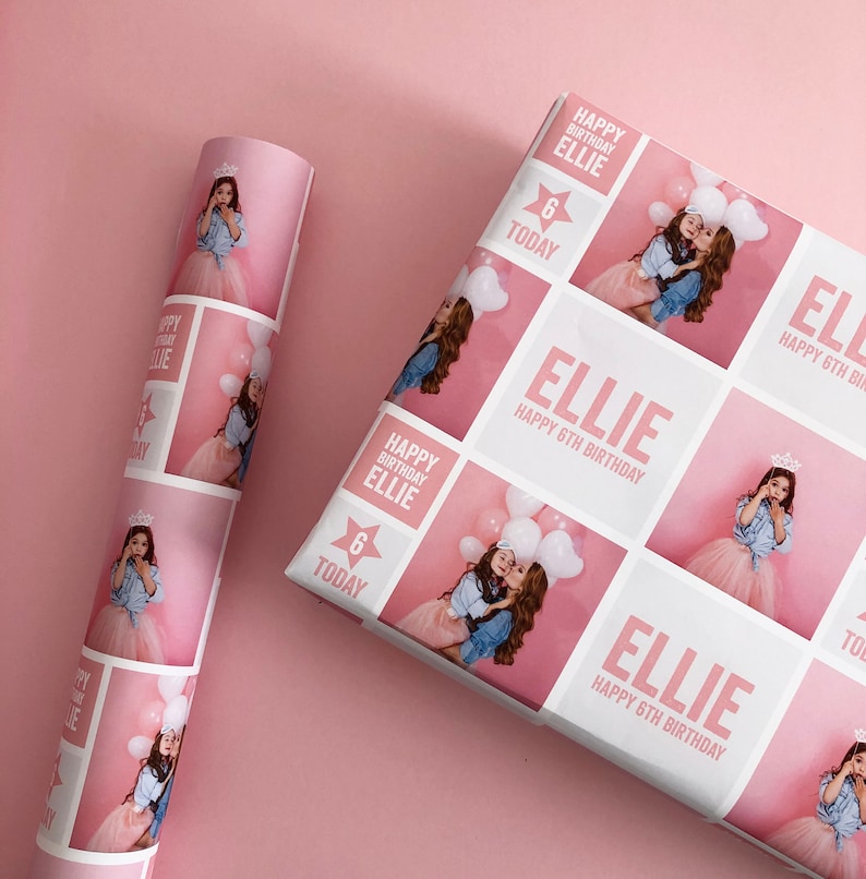 May include: Custom birthday wrapping paper featuring a repeating grid pattern of pink and white squares. The design includes photographs of a child, the text "ELLIE HAPPY 6TH BIRTHDAY," and a star graphic with the text "6 TODAY" in pink and white.
