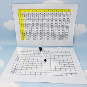 May include: A white dry-erase board with a grid of 12 rows and 12 columns. The board is blank except for the numbers 1 through 12 printed along the top and left side. A white dry-erase marker is lying on the board.