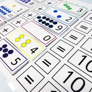 May include: A white sheet of paper with black lines and numbers printed on it. There are also colorful cards with dots and numbers on them. The cards are arranged in a grid pattern. The text on the cards reads "hand- 3 + 2 = 1+ 10 + 8+ 0 6 = 884 = 5 = 10 10".