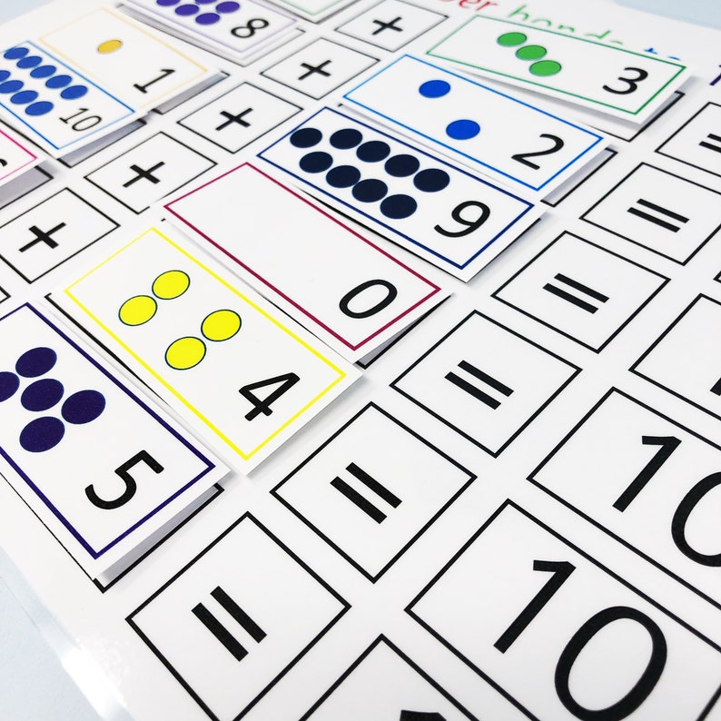 May include: A white sheet of paper with black lines and numbers printed on it. There are also colorful cards with dots and numbers on them. The cards are arranged in a grid pattern. The text on the cards reads "hand- 3 + 2 = 1+ 10 + 8+ 0 6 = 884 = 5 = 10 10".