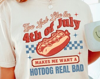 May include: A white t-shirt with a vintage-style graphic that says "You Look Like the 4th of July" with a hot dog illustration and the text "Makes Me Want A Hotdog Real Bad".