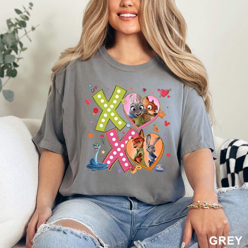 May include: A grey t-shirt featuring the characters from Zootopia. The design includes the letters "XO" in green and pink, with heart-shaped frames containing the characters. A blue snake and other small graphics complete the design.