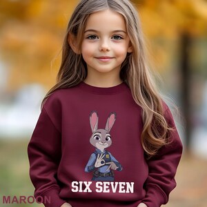 May include: Maroon sweatshirt featuring a cartoon image of Judy Hopps from Zootopia. The text "SIX SEVEN" is printed in white below the image. The word "MAROON" is printed in the lower left corner.
