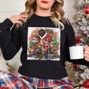 Op de afbeelding: Zwarte crewneck sweatshirt met een kleurrijke kerstillustratie van animatiefiguren. De afbeelding bevat een stier, een luiaard, een konijn en andere personages, omringd door cadeaus en feestelijke versieringen. Het woord "BLACK" staat onderaan.