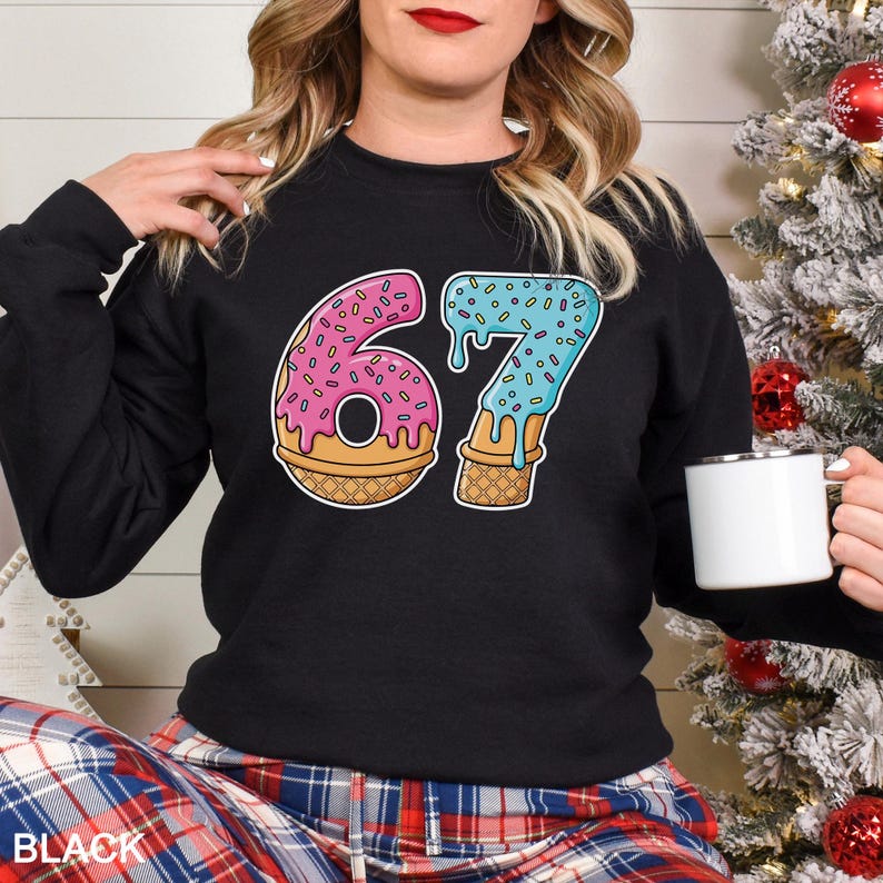 May include: Black sweatshirt with a colorful graphic of the number "67" designed as a donut and ice cream cone. The number "6" is a pink donut with sprinkles, and the "7" is blue ice cream dripping down a cone. The word "BLACK" is printed at the bottom.