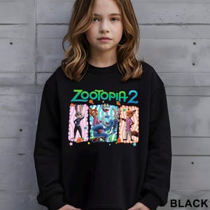 Puede incluir: Sudadera negra con el texto "ZOOTOPIA 2" en verde y azul. El gr&aacute;fico incluye personajes de dibujos animados en marcos rectangulares coloridos. La palabra "BLACK" est&aacute; impresa en blanco en la parte inferior derecha.