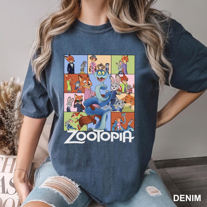 May include: A denim blue t-shirt featuring a colorful graphic from the animated movie "Zootopia." The design includes various characters in a grid layout, with the word "Zootopia" in white block letters.