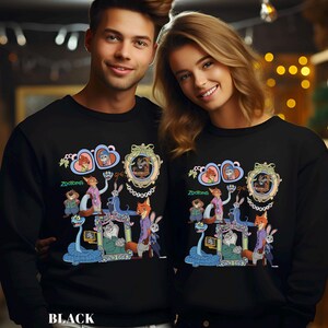 May include: Black sweatshirt with a vibrant Zootopia-themed graphic. The design showcases characters such as Nick Wilde and Judy Hopps, set within decorative frames. The word "Zootopia" is written in green below the central image.