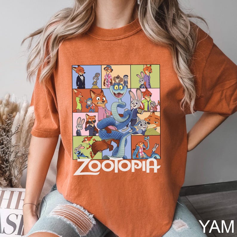 May include: Burnt orange t-shirt featuring a colorful graphic from the animated movie "Zootopia." The design includes various characters in a grid layout, with the movie title in white block letters. The shirt has short sleeves.