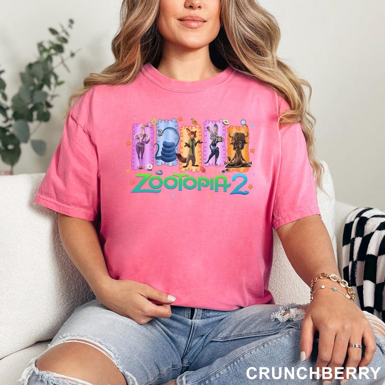 K&ouml;nnte beinhalten: Ein leuchtend pinkfarbenes Kurzarm-T-Shirt mit einem Grafikdruck von f&uuml;nf animierten Charakteren aus Zootopia 2. Das Design enth&auml;lt den Schriftzug Zootopia 2 in t&uuml;rkisfarbenen Buchstaben unter den Charakteren, die in bunten Rechtecken eingerahmt sind.